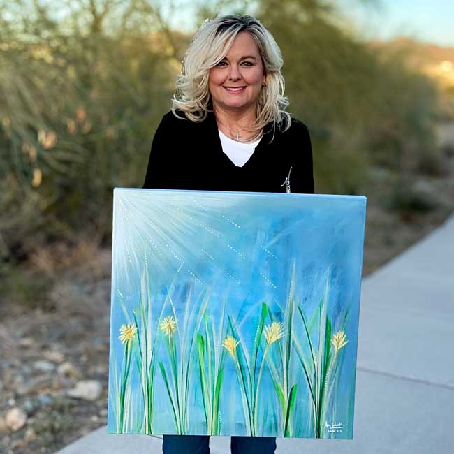 Amy Schultz holding one of her original paintings outdoors
